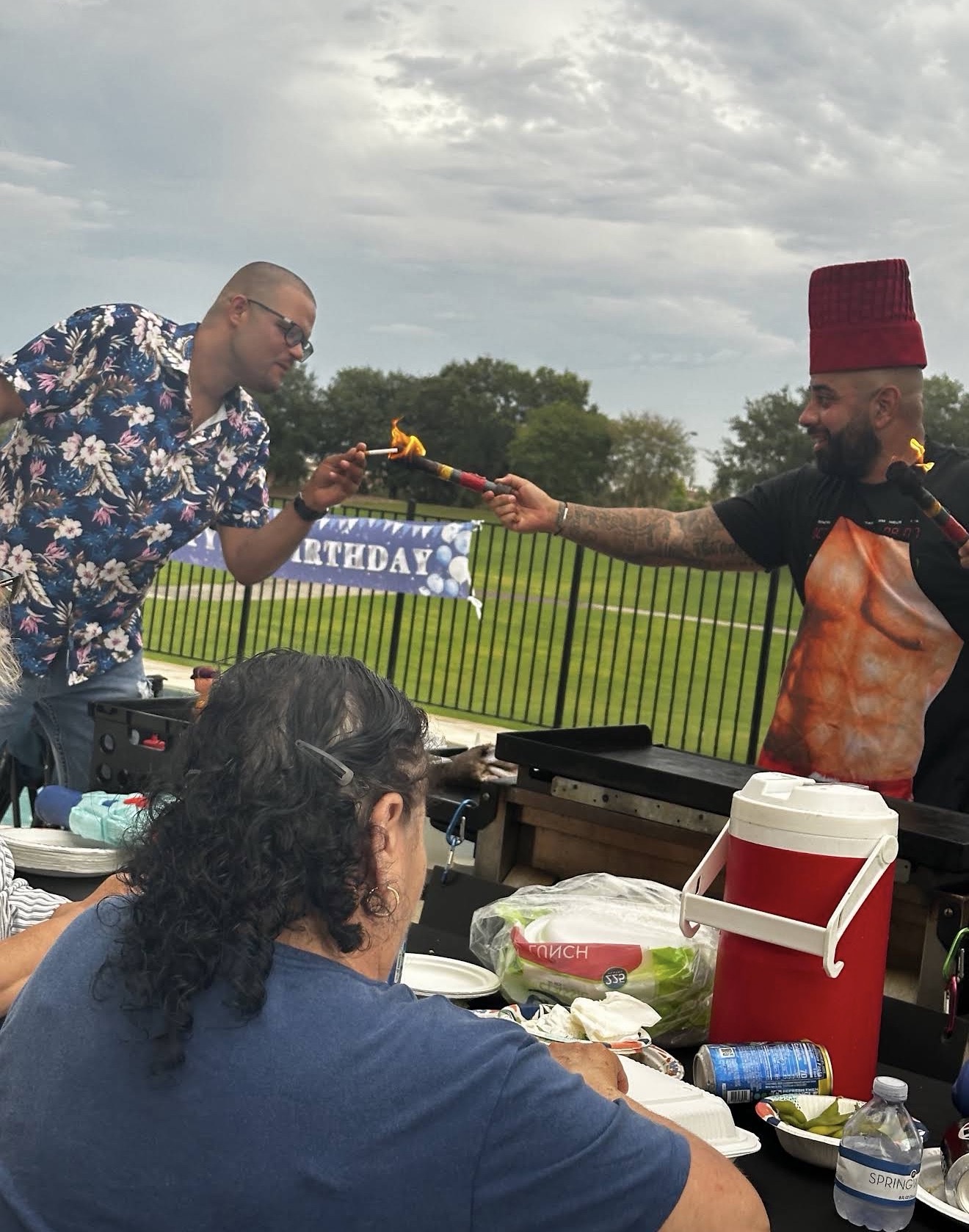 Chef in a red hat and funny muscle apron lighting a guest's cigarette with a flaming sword at a Florida birthday party
