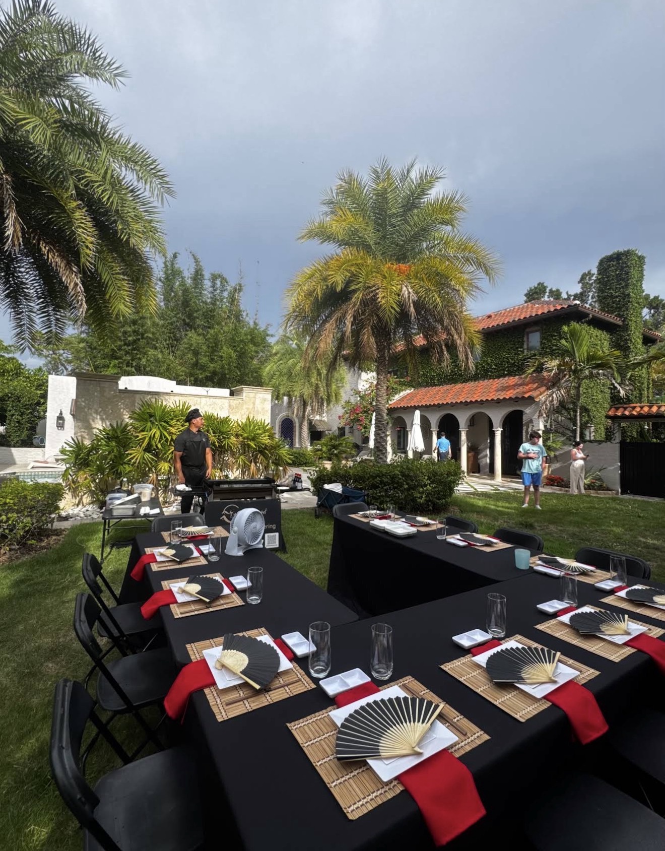 Elegant backyard hibachi setup with black tablecloths, fans and palm trees in front of a villa in Florida