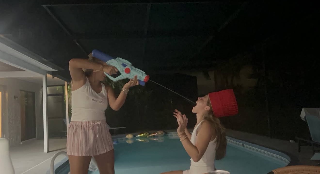 Two guests playing the sake squirt gun game by the pool at night in Florida, one wearing the red chef hat