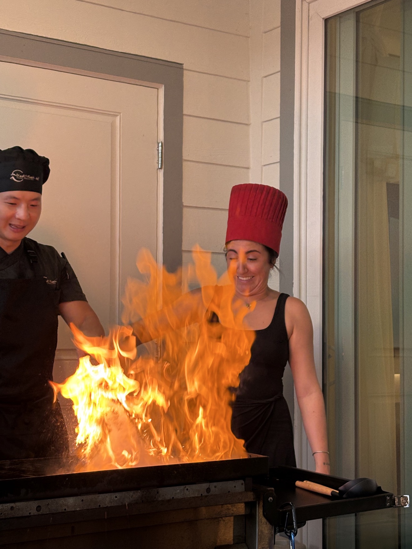 Guest wearing the red chef hat cooking with a big flame burst, guided by the chef in Florida